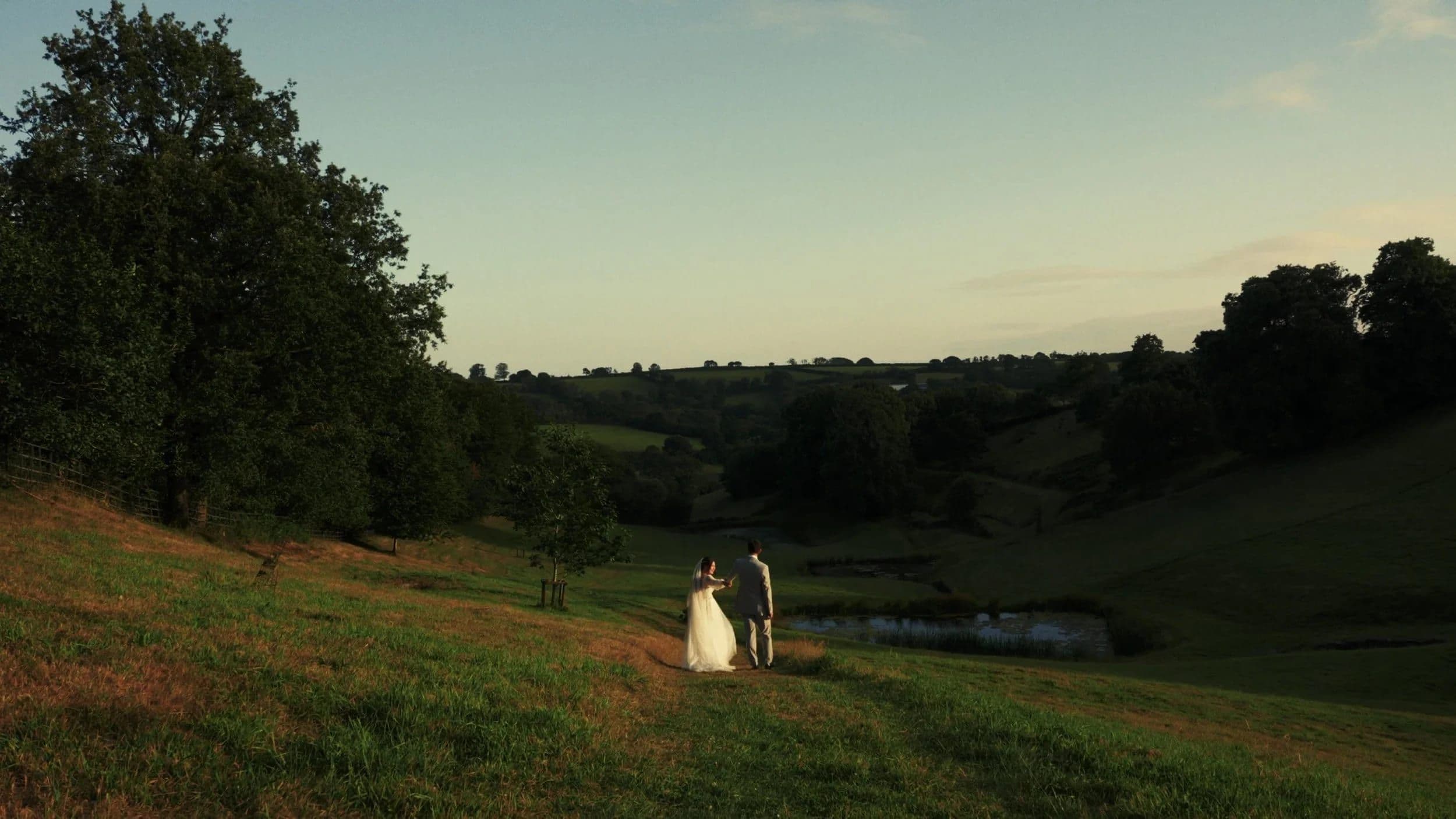 Andrew and Ali walking down a sunlit valley towards a lake, in a still from their wedding film