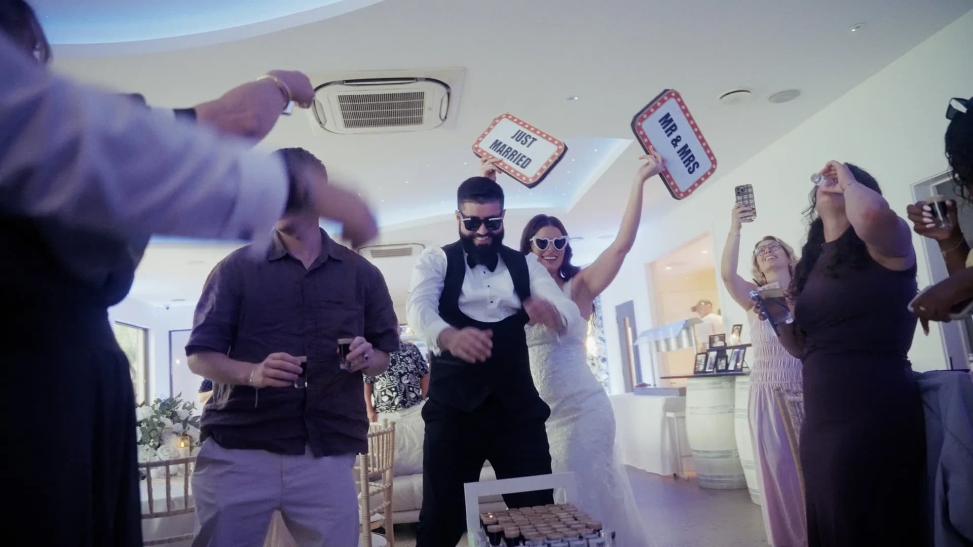 Grace & Matt dancing in sunglasses, holding up Just Married and Mr & Mrs signs as guests cheer around them